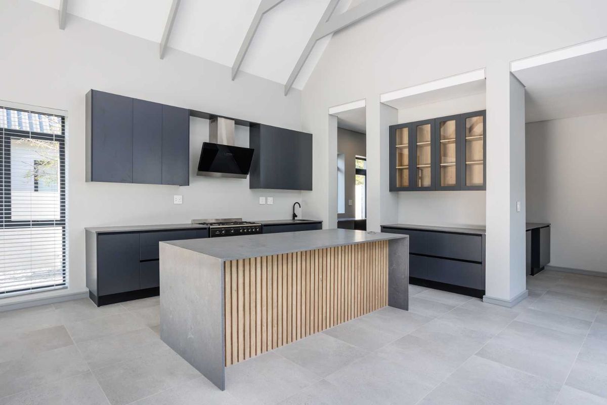 Modern kitchen featuring a central island with timber slat detailing, dark cabinetry, high vaulted ceilings, and sleek tiled flooring in a contemporary open-plan layout.