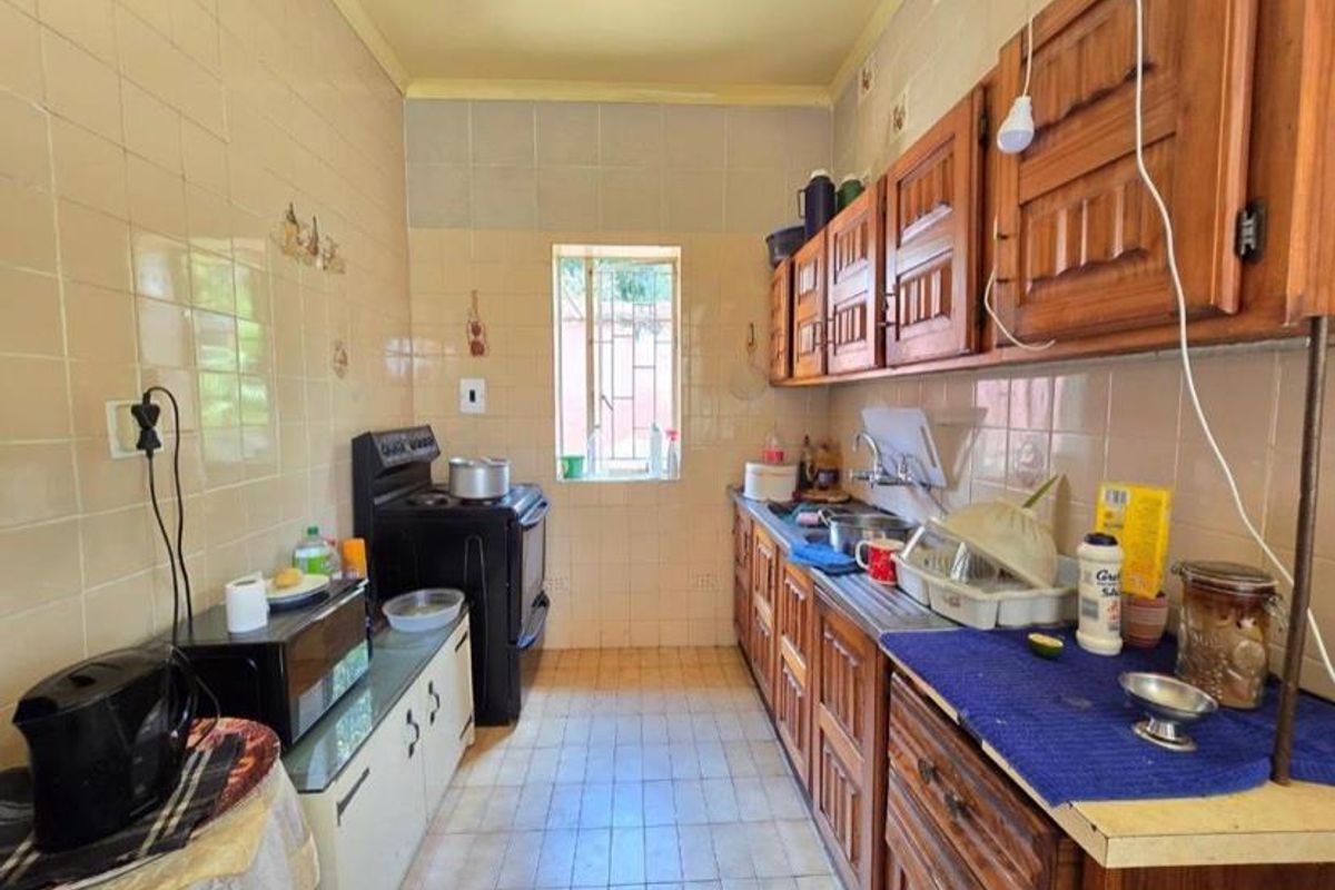 A dated galley-style kitchen featuring wooden cabinetry, tiled walls, and a functional layout with a freestanding stove and sink area.