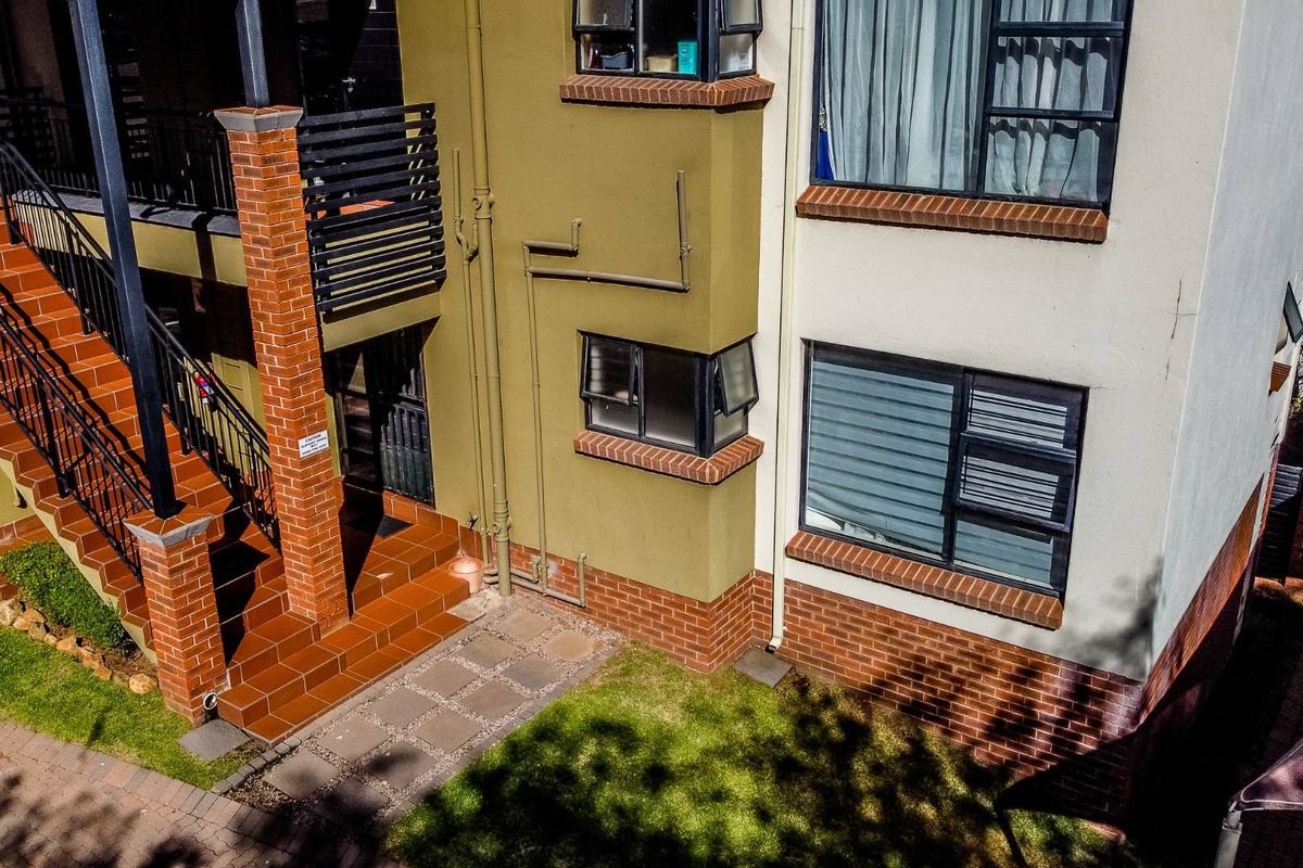 An elevated view of the apartment building exterior, featuring brick accents, tiled staircases, and metal balustrades with access to ground level garden space.