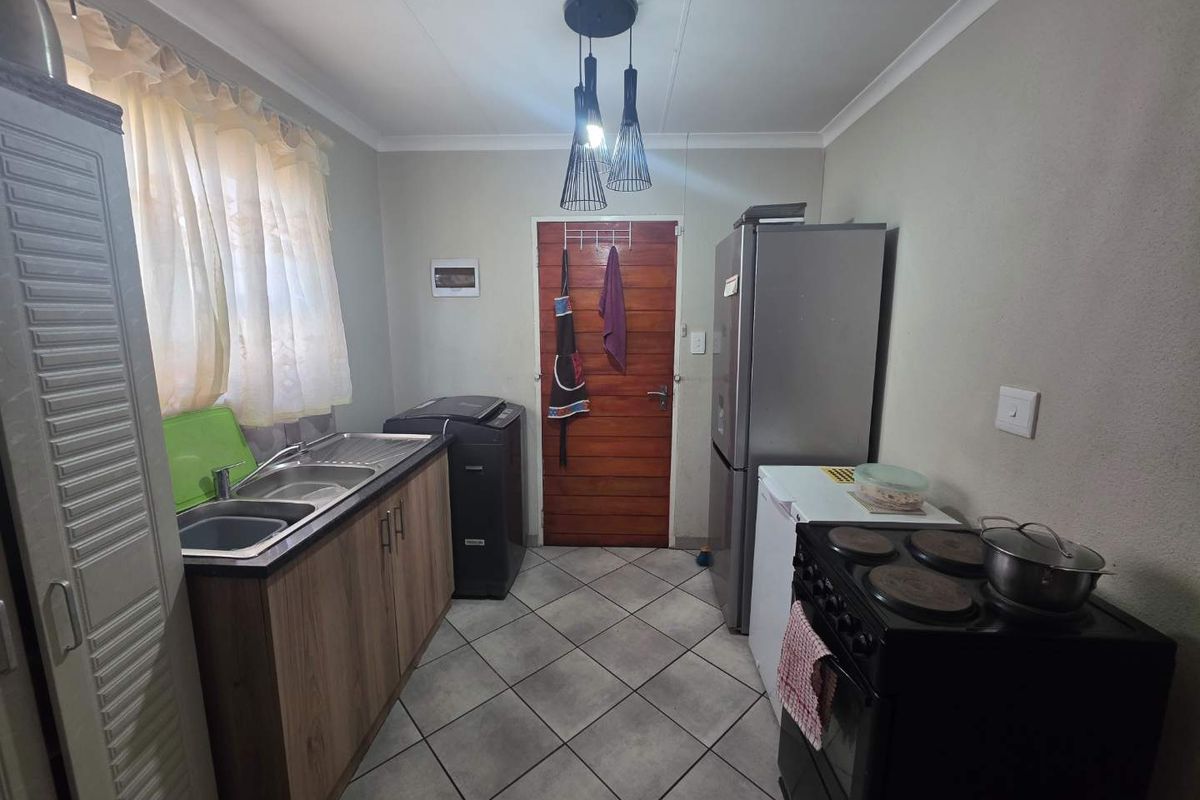 A functional kitchen featuring tiled flooring, built-in cabinetry, a double sink, and a freestanding stove, providing a practical workspace for daily cooking and laundry needs.