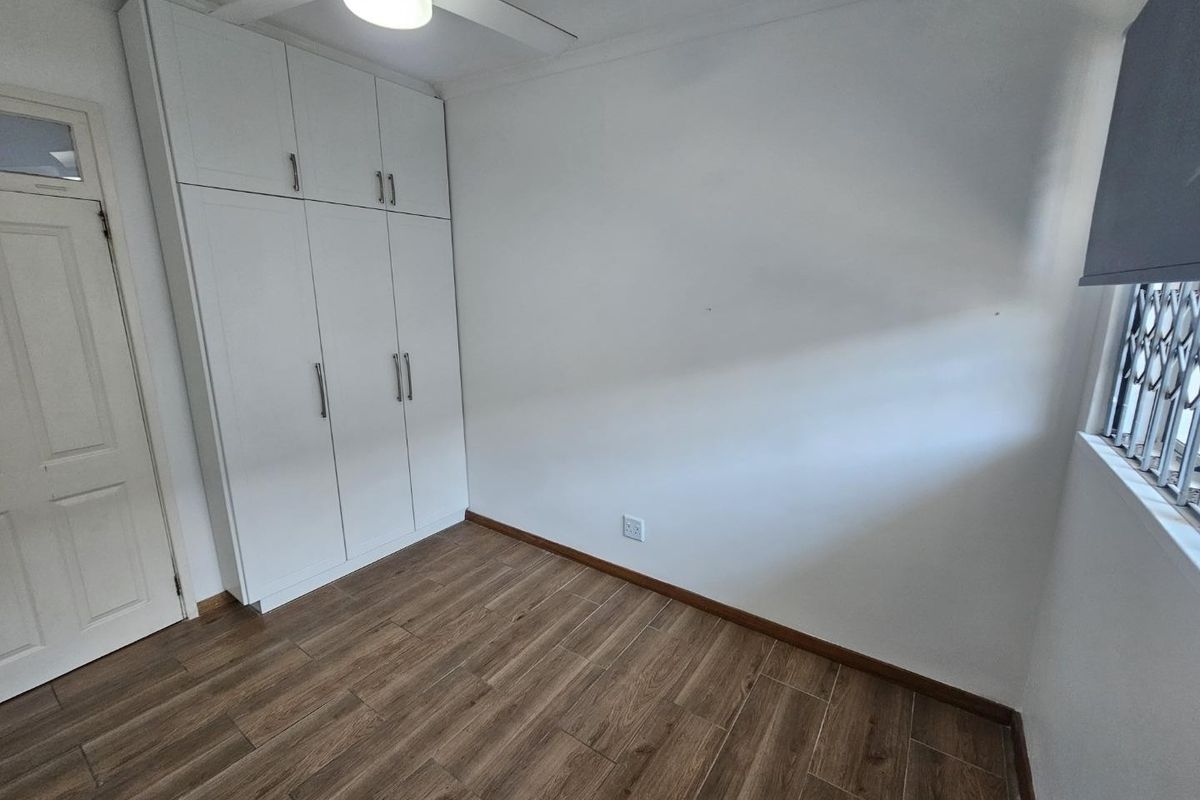 A clean, empty bedroom featuring modern laminate flooring, built-in cupboards, and a ceiling fan, offering a neutral space ready for personalization.