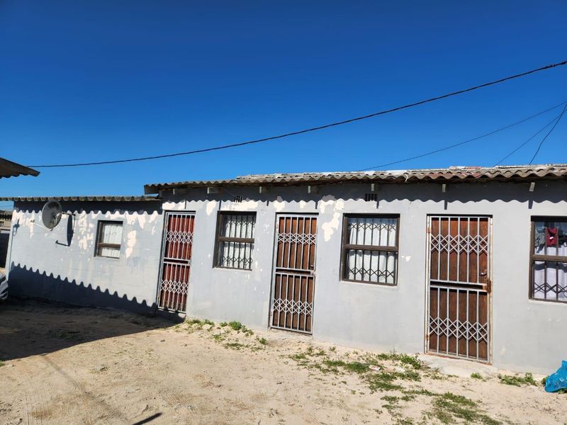 Rear exterior view of the property featuring multiple access points with security gates and bars, showing signs of weathered exterior paint.