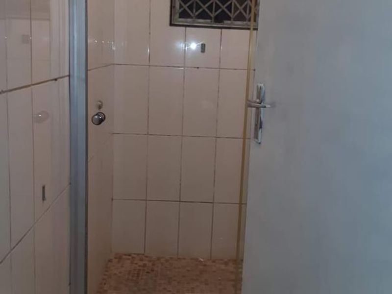 A compact bathroom featuring a shower enclosure with tiled walls and floor, a toilet, and a window with a security gate.
