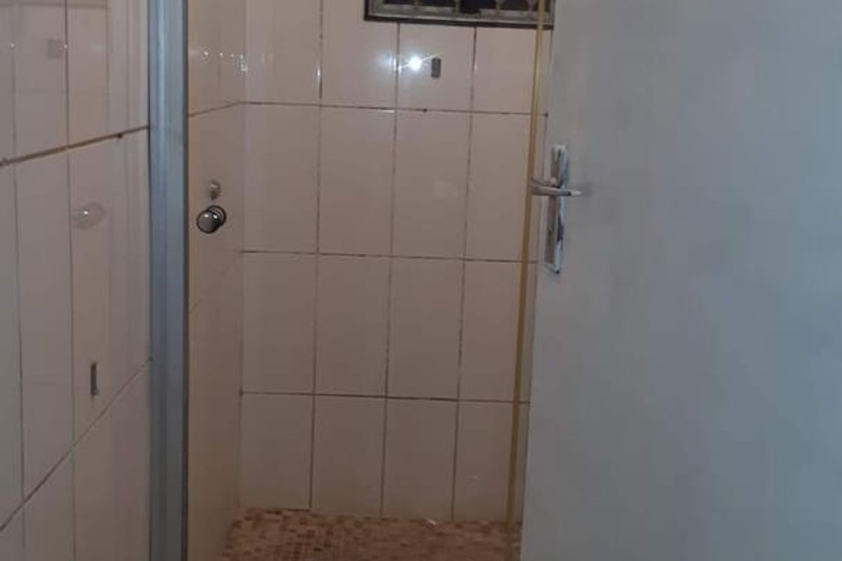 A compact bathroom featuring a shower enclosure with tiled walls and floor, a toilet, and a window with a security gate.