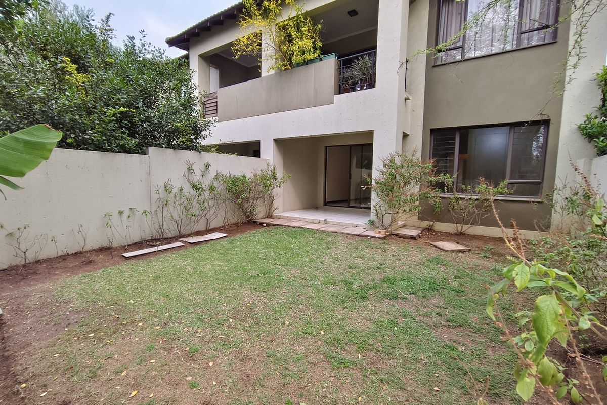 Rear view of the apartment building featuring a private garden, a ground-floor patio, and an upper-level balcony with sliding door access.