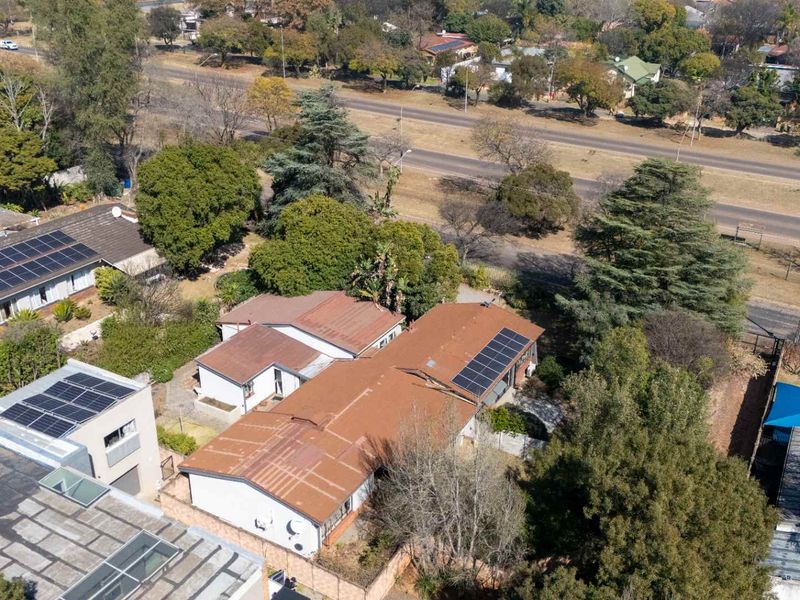 Aerial view of the property featuring multiple roof sections with installed solar panels, surrounding garden space, and boundary walls.
