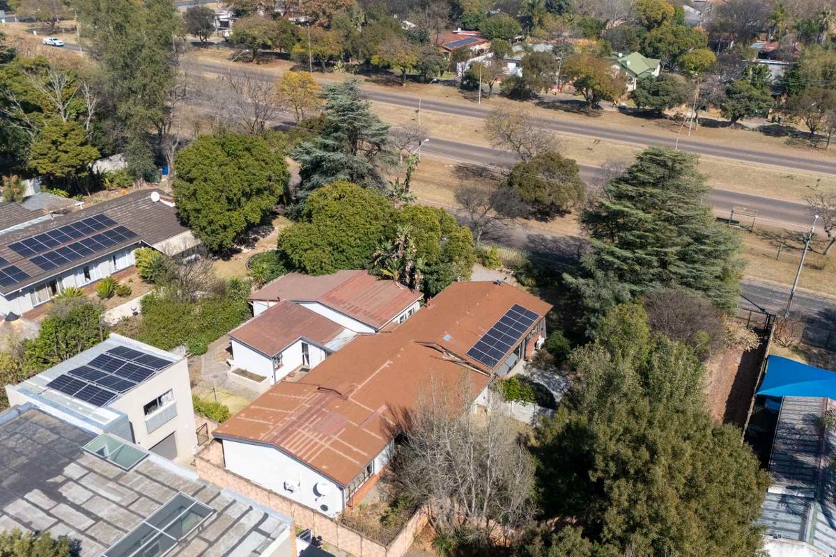 Aerial view of the property featuring multiple roof sections with installed solar panels, surrounding garden space, and boundary walls.