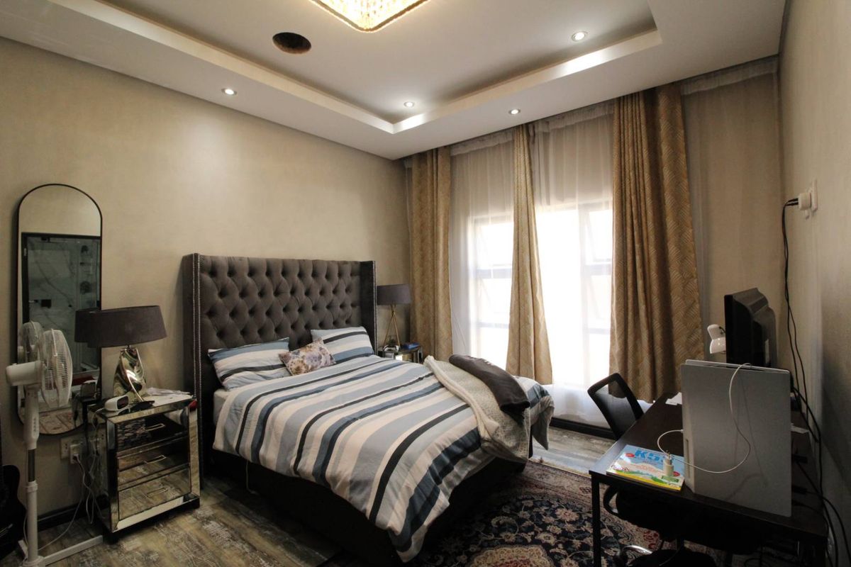 A well-appointed bedroom featuring a tray ceiling with recessed lighting, large windows with curtains, and wood-look flooring.