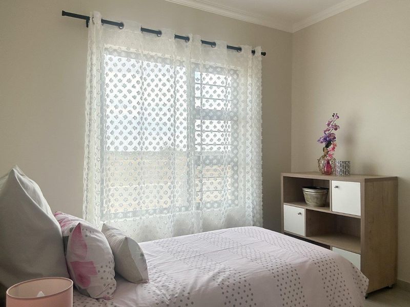 A well-lit bedroom featuring neutral wall tones and a large window with a curtain rod.