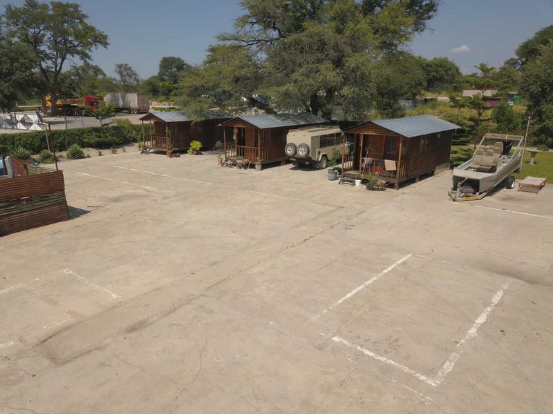 Aerial view of a commercial property featuring multiple wooden cabins situated on a large concrete parking lot with marked bays.