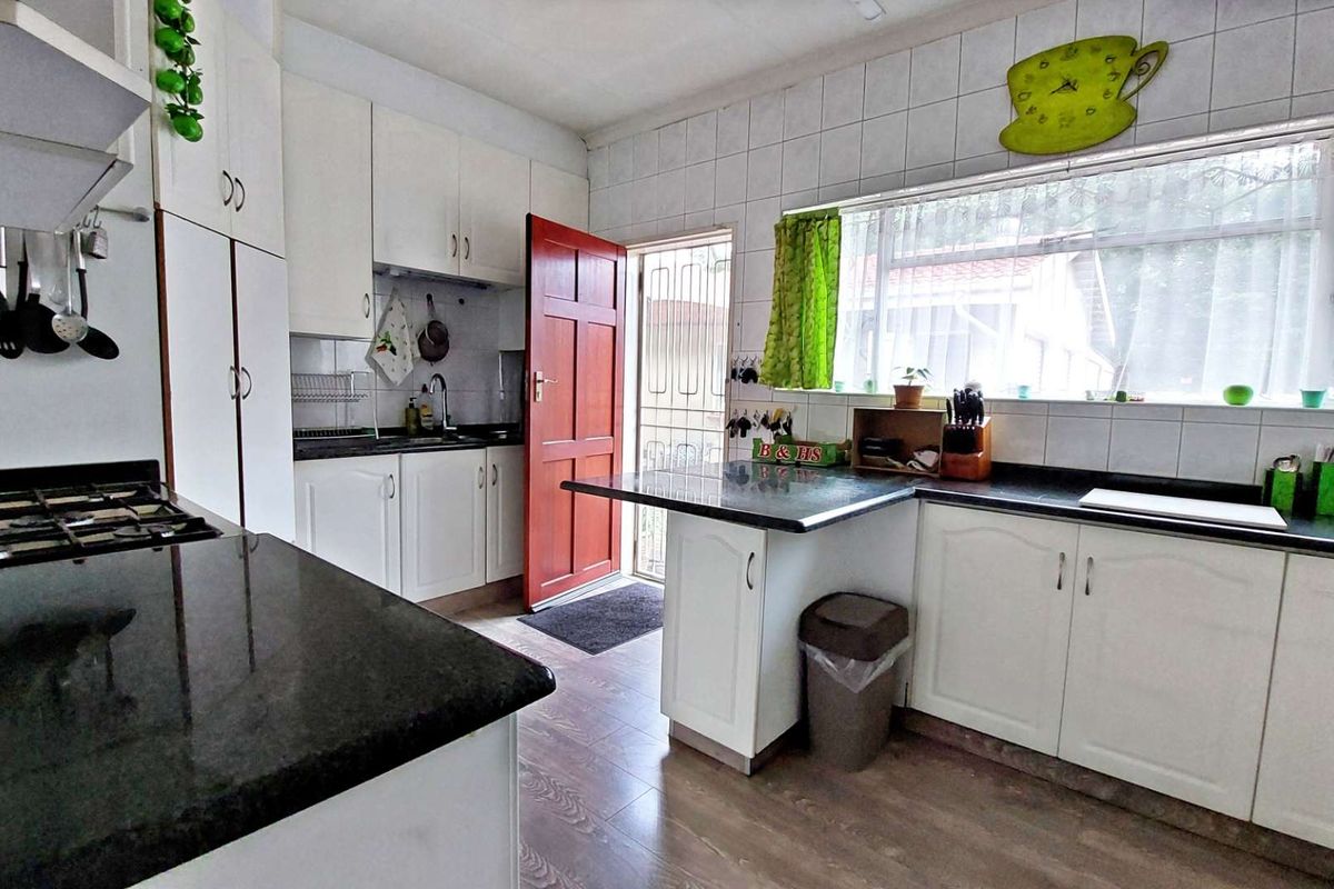 A functional kitchen featuring white cabinetry, dark granite countertops, a gas hob, and tiled splashbacks with direct access to the exterior.