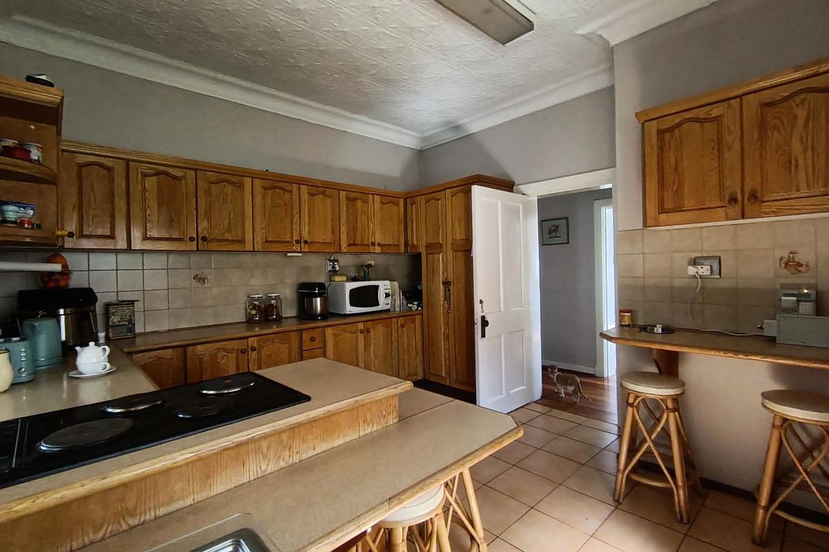 A functional kitchen featuring traditional wooden cabinetry, laminate countertops, an integrated electric hob, and tiled flooring with a neutral backsplash.