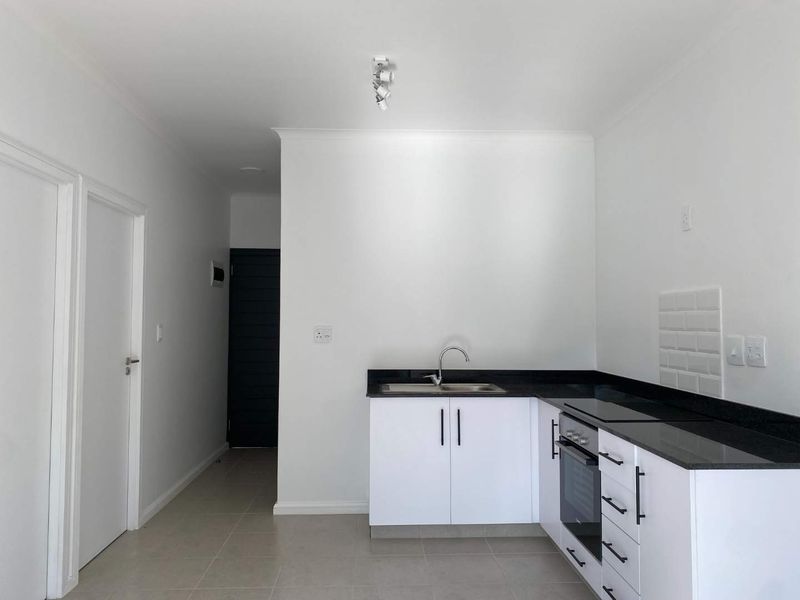 A clean, modern kitchen featuring white cabinetry, dark granite countertops, a built-in oven, and a subway tile backsplash.