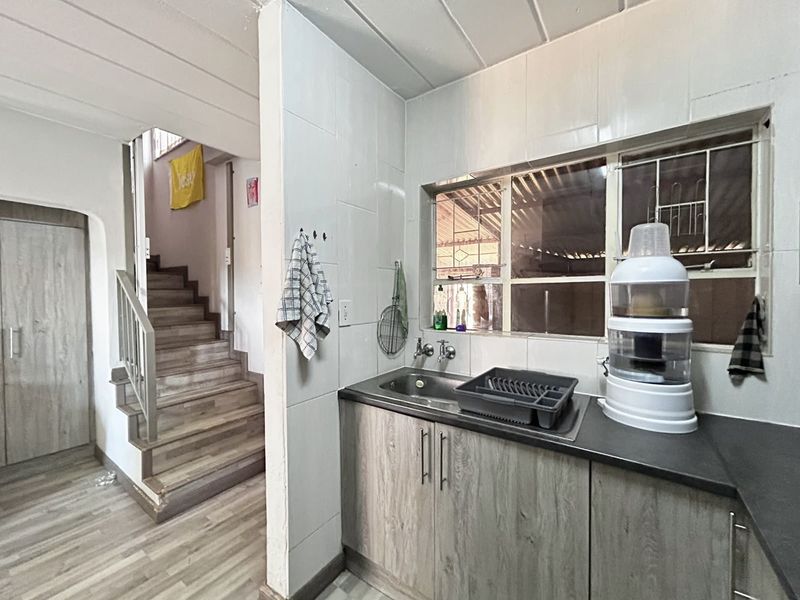 A functional kitchen area featuring laminate cabinetry and a stainless steel sink, adjacent to a staircase with timber-look flooring.