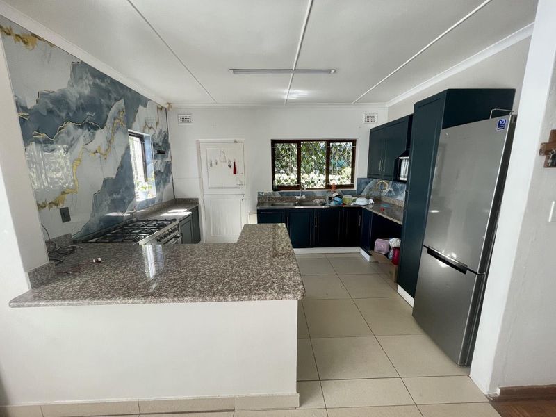 A functional kitchen featuring dark cabinetry, granite countertops, a gas stove, and decorative wall paneling, offering a practical layout with ample workspace.