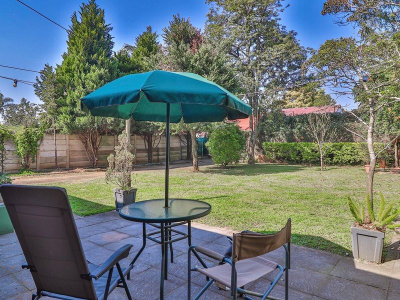 A private backyard featuring a paved patio area, established lawn, mature trees, and perimeter boundary walling.