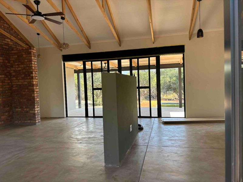 Spacious open-plan living area featuring exposed timber rafters, polished concrete floors, and large black-framed sliding doors opening to the outdoor patio.
