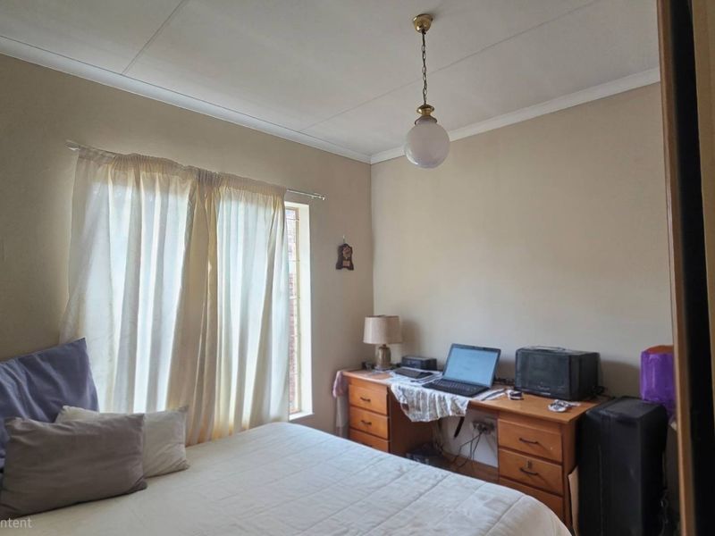 A functional bedroom featuring neutral wall tones, a pendant light fixture, and a window with curtain rod.