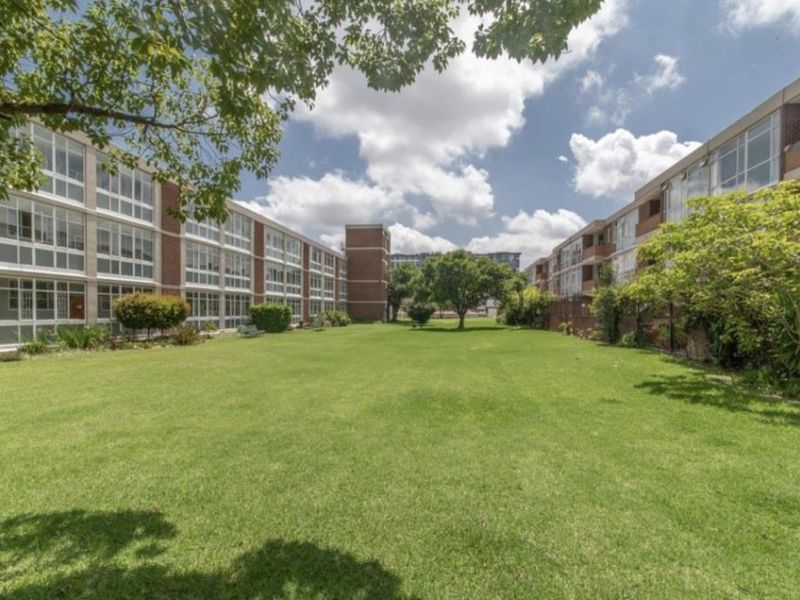 A well-maintained communal garden area situated between two apartment blocks, featuring expansive lawns and mature trees.