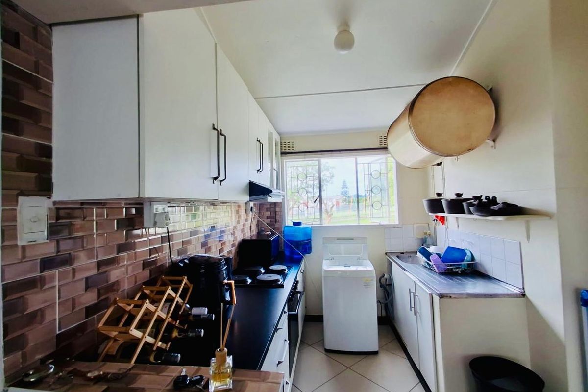 Functional galley-style kitchen featuring built-in cabinetry, tiled backsplash, and a stainless steel sink with natural light from the window.