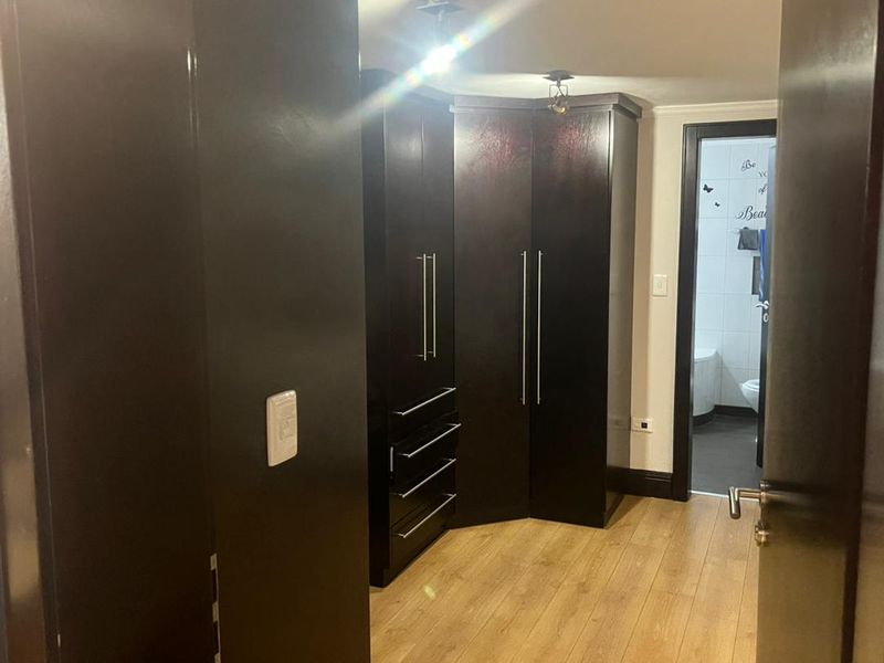 A bedroom area featuring dark wood built-in cupboards, light laminate flooring, and direct access to an en-suite bathroom.