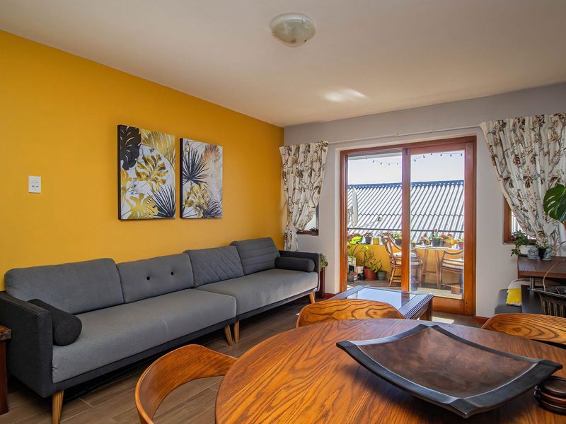 A bright living room featuring a bold yellow accent wall, tiled flooring, and a sliding glass door providing access to an outdoor balcony area.