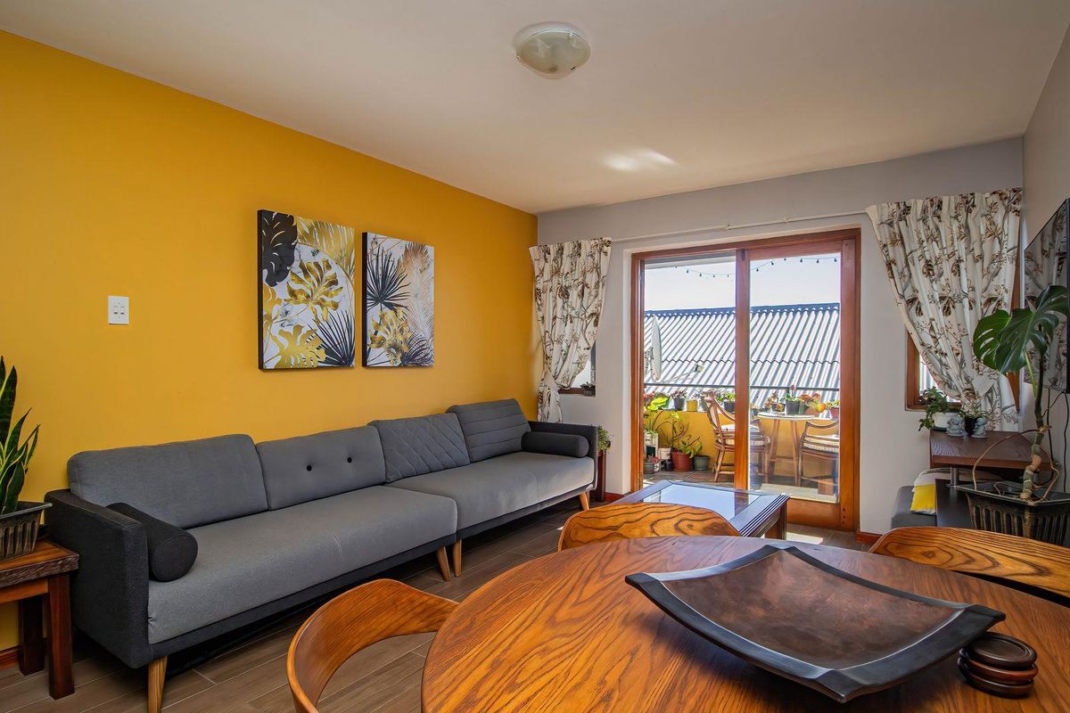 A bright living room featuring a bold yellow accent wall, tiled flooring, and a sliding glass door providing access to an outdoor balcony area.