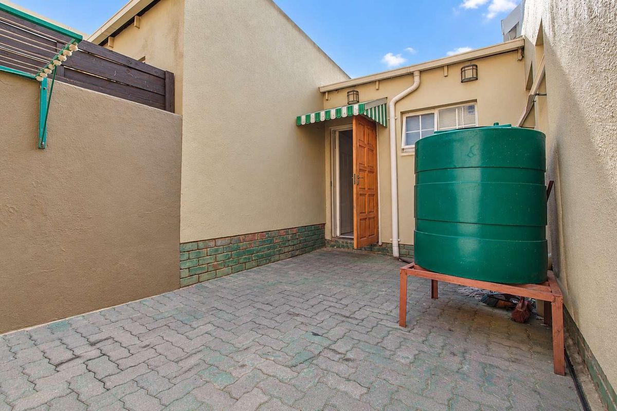A paved rear courtyard featuring a water storage tank, wall-mounted clothesline, and direct access to the property via a side door.
