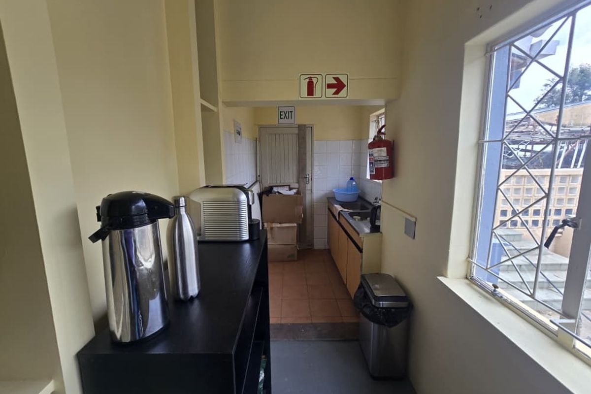 A functional office kitchenette area featuring built-in cabinetry, a sink, and an emergency exit door with safety signage.