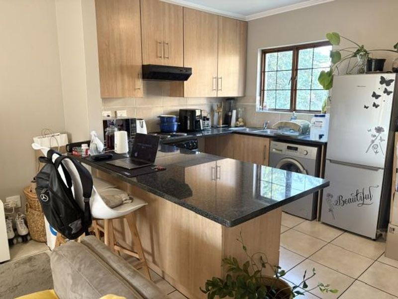 Functional kitchen featuring light wood-tone cabinetry, dark granite countertops, integrated appliances, and tiled flooring with a breakfast bar layout.