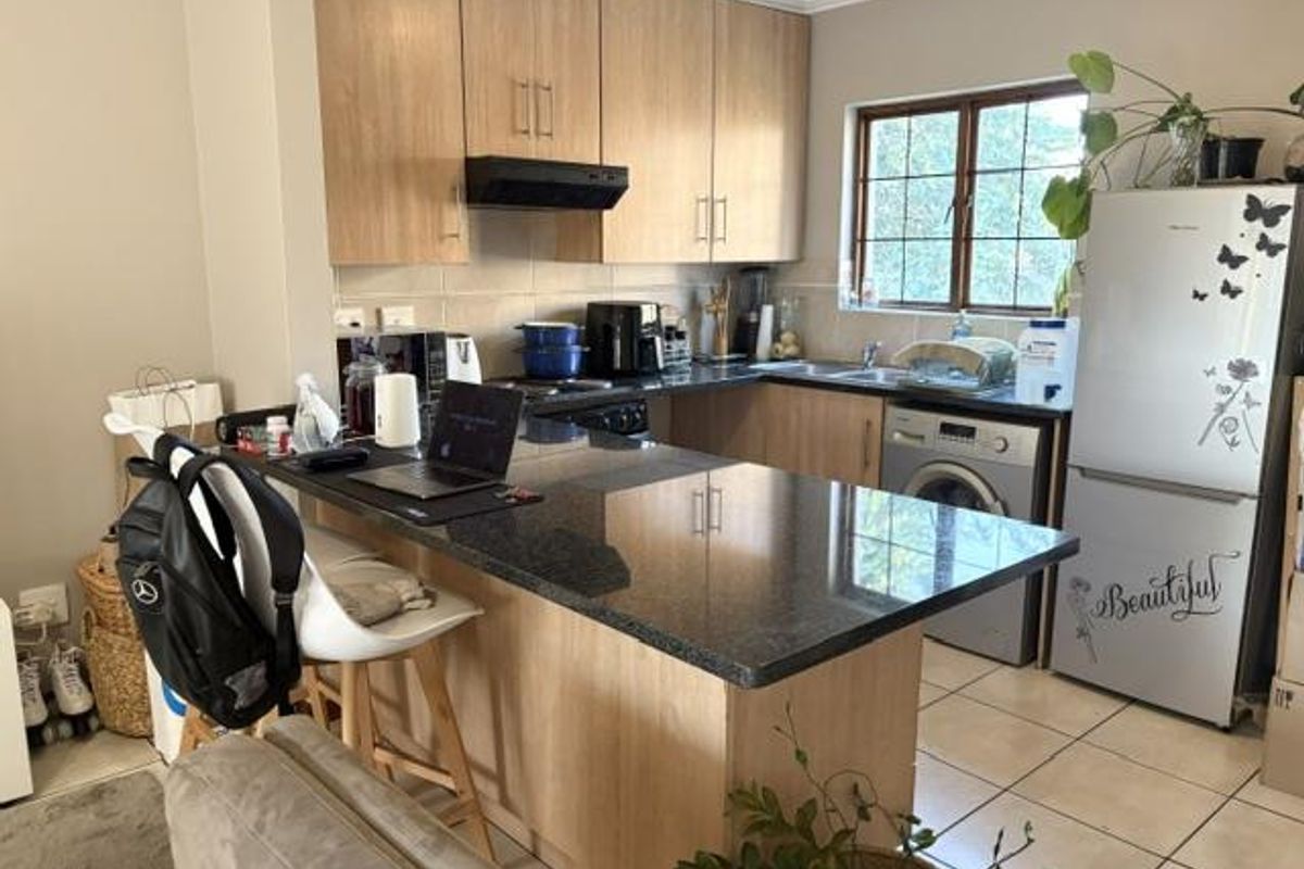 Functional kitchen featuring light wood-tone cabinetry, dark granite countertops, integrated appliances, and tiled flooring with a breakfast bar layout.