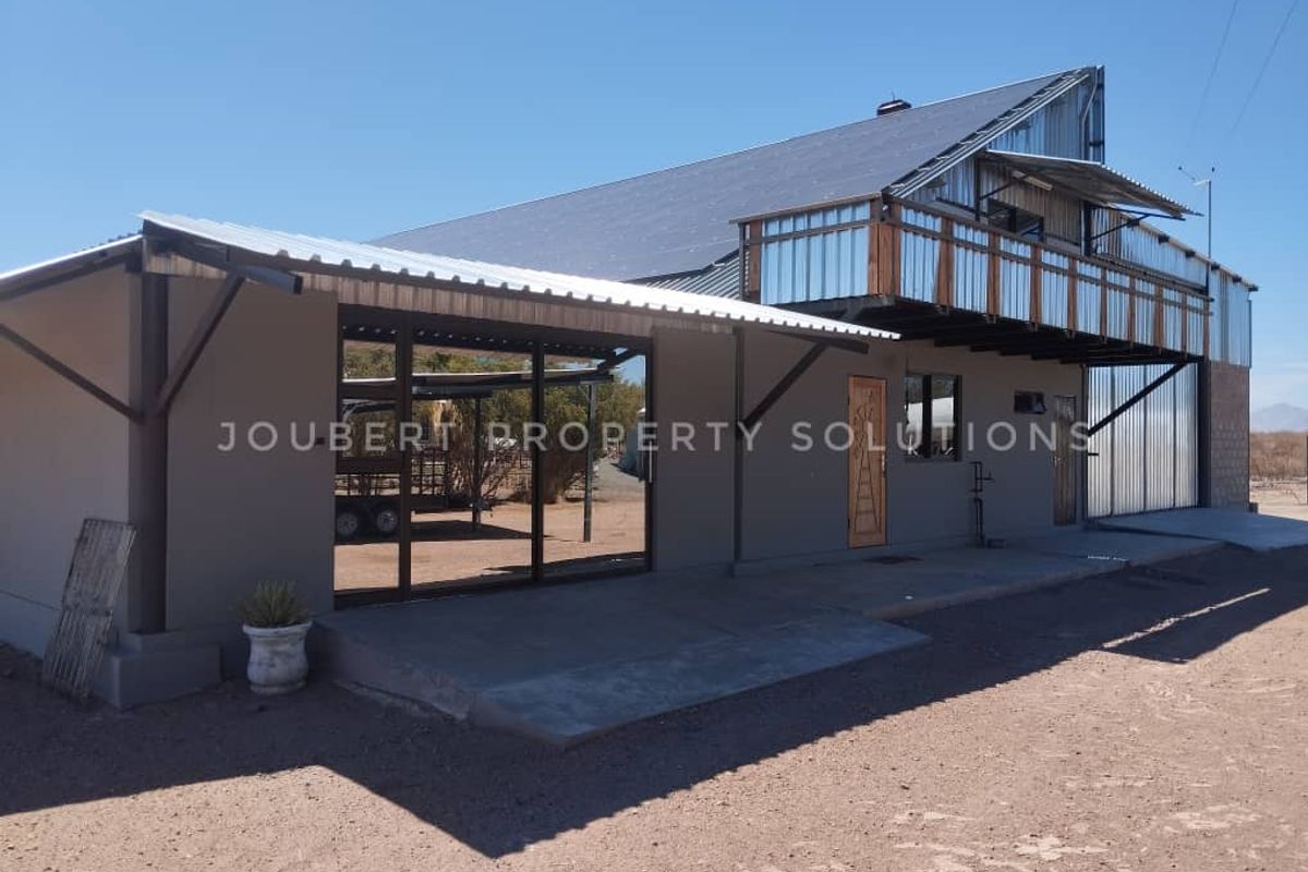 Exterior view of a farm building featuring a covered patio area, metal roofing, and an upper-level balcony with corrugated metal cladding.