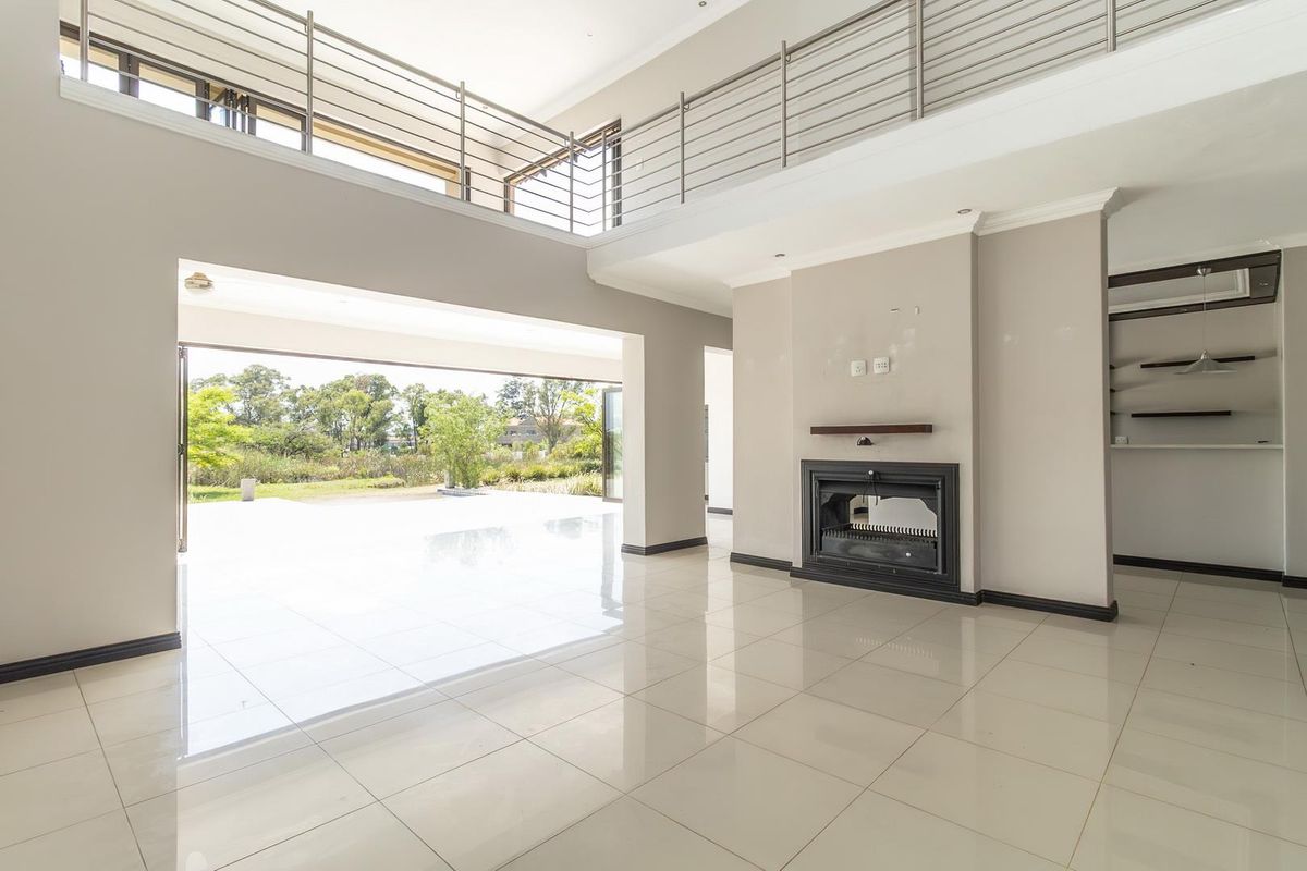 Spacious double-volume living area featuring polished porcelain tiles, a built-in fireplace, and seamless flow to the outdoor patio through large sliding doors.