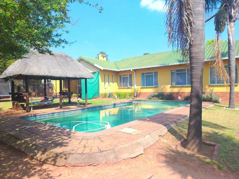 Rear garden area featuring a swimming pool and a traditional thatched lapa, set against the yellow-painted exterior of the house.