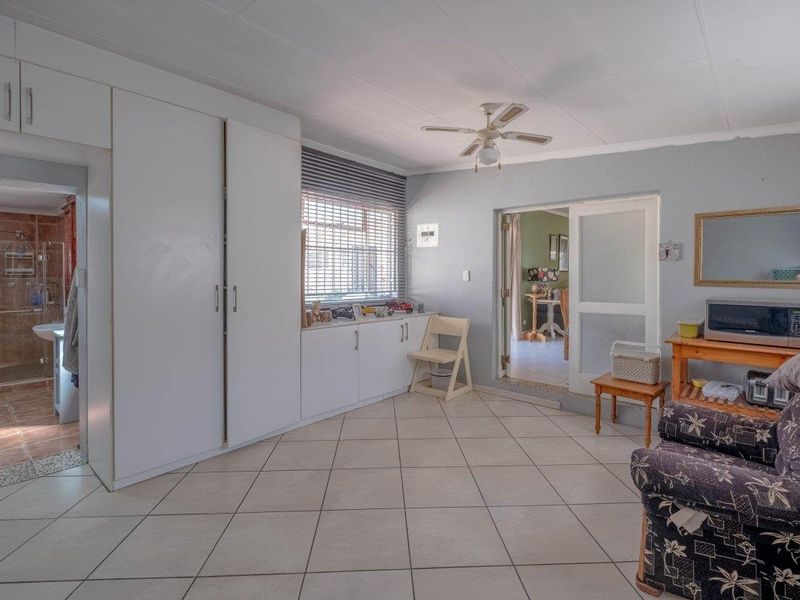 A bedroom featuring built-in cupboards, tiled flooring, and a ceiling fan, with direct access to an en-suite bathroom.