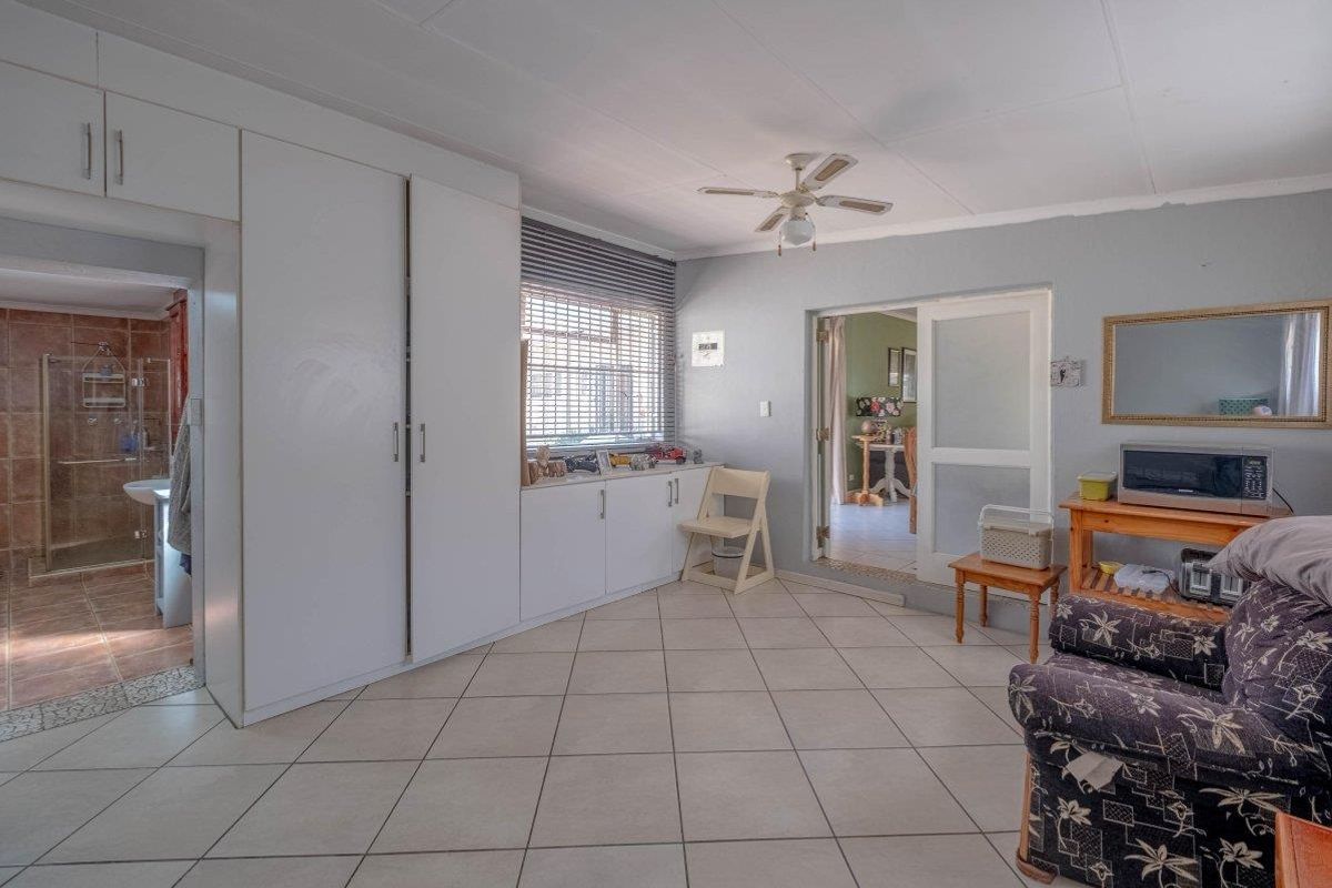 A bedroom featuring built-in cupboards, tiled flooring, and a ceiling fan, with direct access to an en-suite bathroom.
