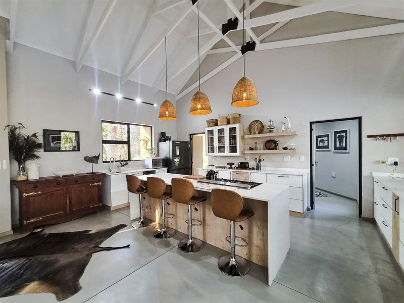 Spacious open-plan kitchen featuring a large island with stone countertops, gas cooktop, vaulted ceilings with exposed trusses, and modern polished concrete flooring.