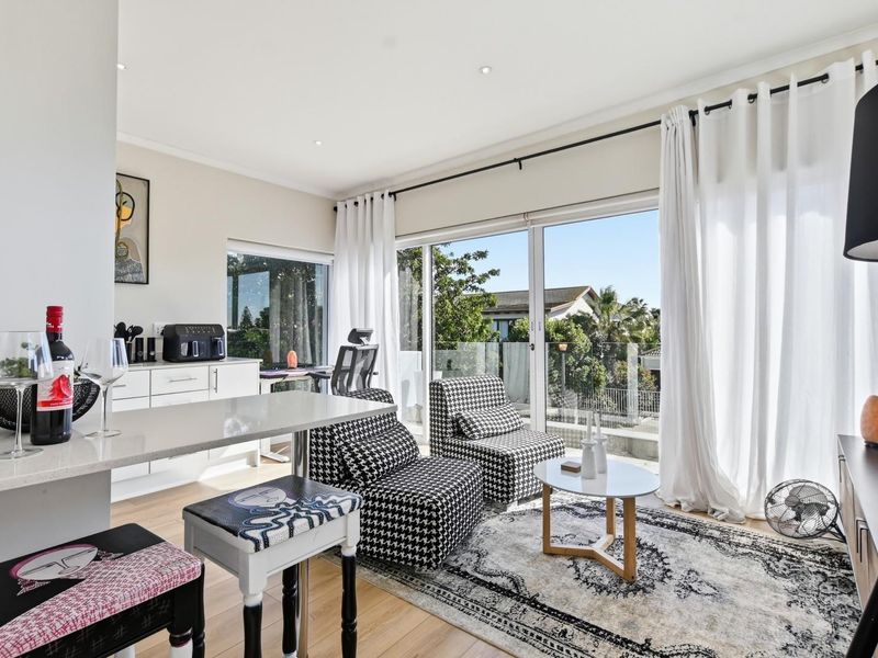 Bright open-plan living area featuring modern laminate flooring, recessed lighting, and large sliding glass doors leading to a balcony with a glass balustrade.