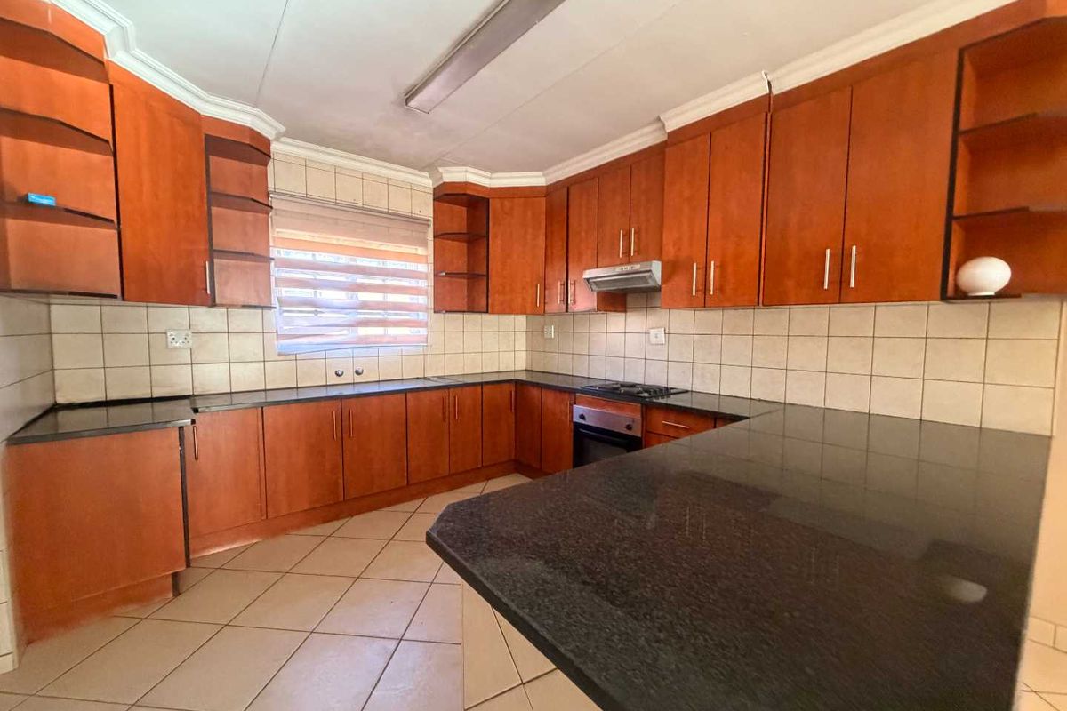 A functional kitchen featuring wooden cabinetry, granite countertops, built-in oven, gas hob, and tiled finishes throughout.