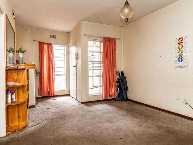 A vacant living area featuring built-in shelving, security bars on windows, and carpet flooring, offering a blank canvas for renovation and modernization.