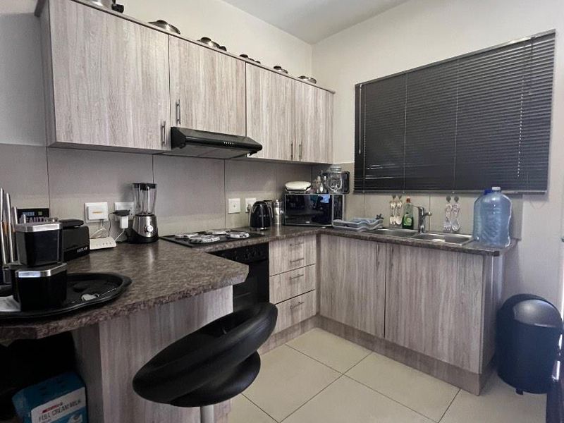A functional kitchen featuring light wood-grain cabinetry, dark laminate countertops, built-in cooking appliances, and tiled flooring with a window overlooking the exterior.