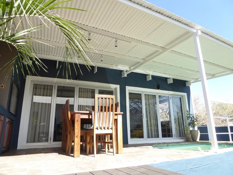 A covered patio area featuring a corrugated metal roof, track lighting, and stone paving, providing direct access to the swimming pool through sliding glass doors.