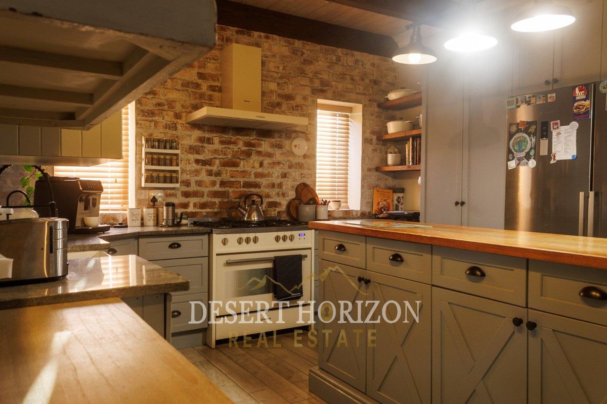 A charming kitchen featuring exposed brick walls, a central island with a wooden countertop, shaker-style cabinetry, and a built-in gas range with extractor fan.