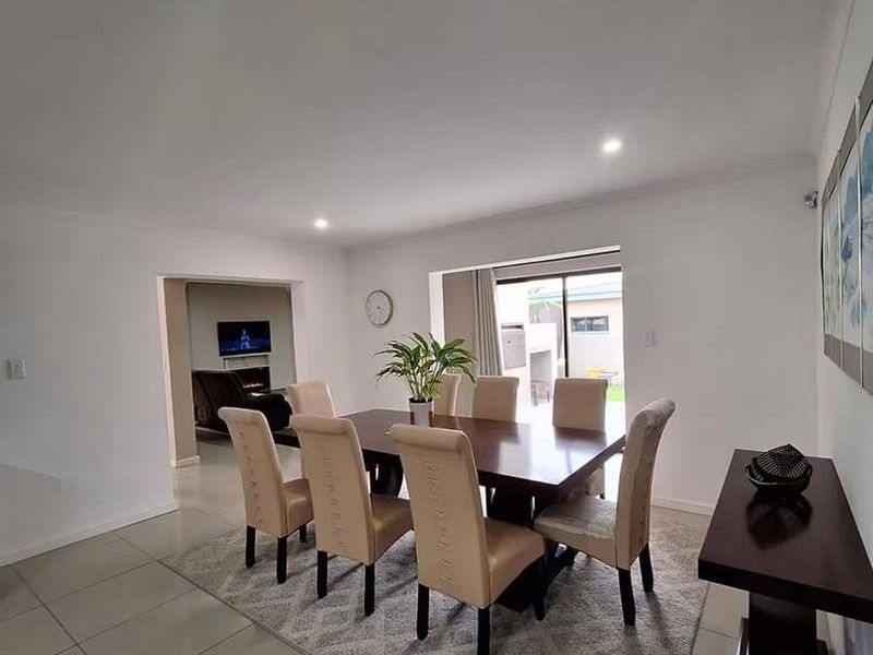 A bright and spacious dining area featuring neutral tiled flooring, recessed downlighting, and direct access to the outdoor patio through a sliding glass door.
