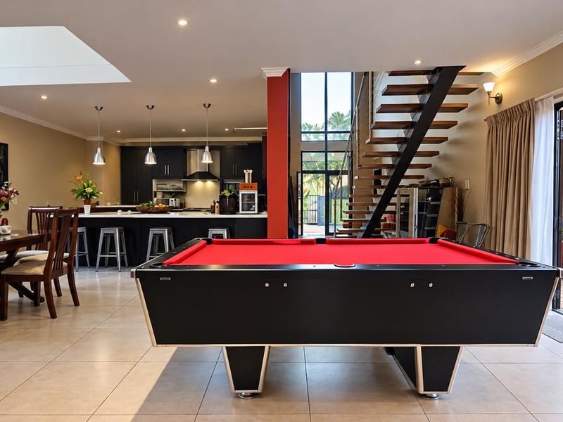 Spacious open-plan living area featuring a modern kitchen with island, sleek cabinetry, and a striking staircase, seamlessly connecting to the outdoor patio.