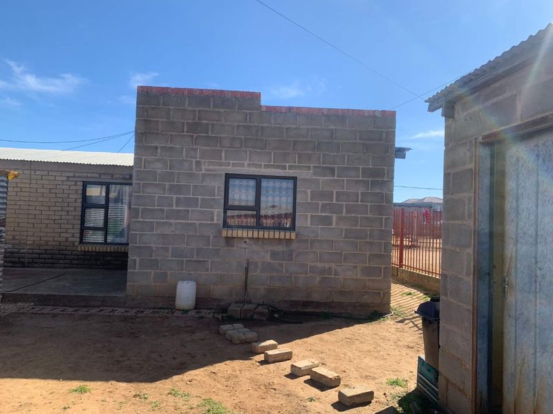 Rear view of a residential property featuring concrete block construction, aluminium window frames, and an unpaved yard area.