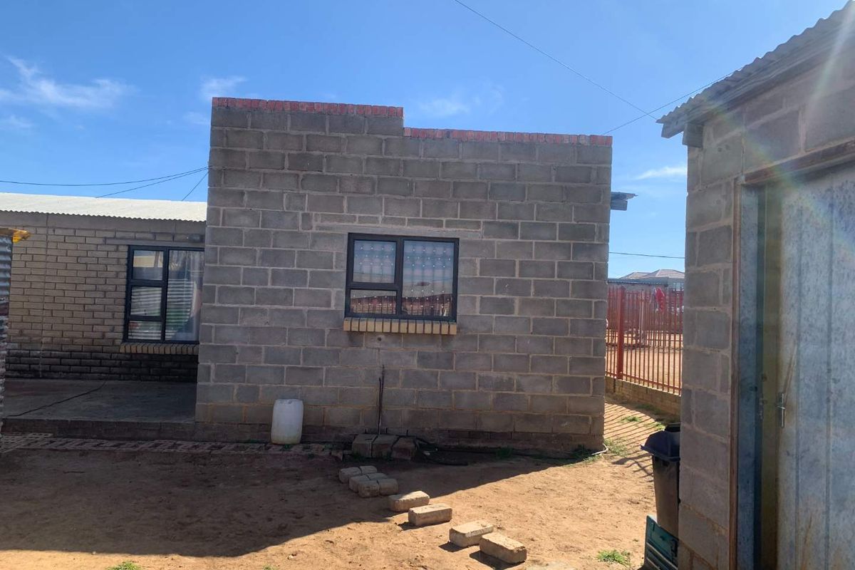 Rear view of a residential property featuring concrete block construction, aluminium window frames, and an unpaved yard area.