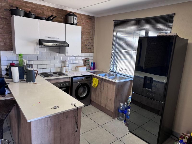 Modern kitchen featuring white upper cabinetry, wood-look lower cabinets, stone countertops, subway tile backsplash, and an exposed brick feature wall.