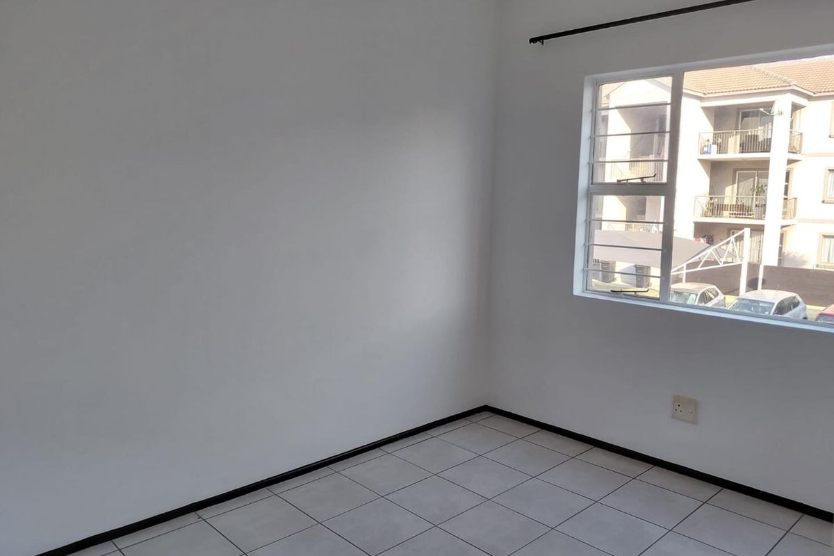 A bright, empty bedroom featuring neutral tiled flooring, white walls, and a window fitted with security bars.