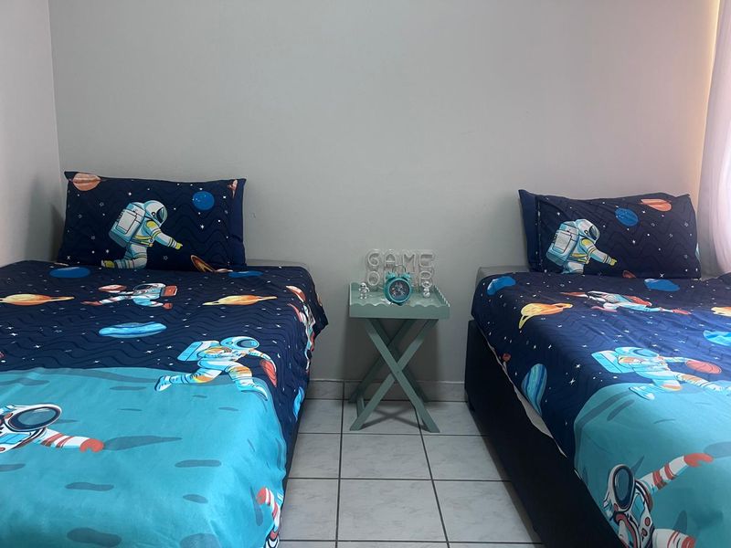 A bedroom featuring tiled flooring, currently set up with two twin beds and a central side table.